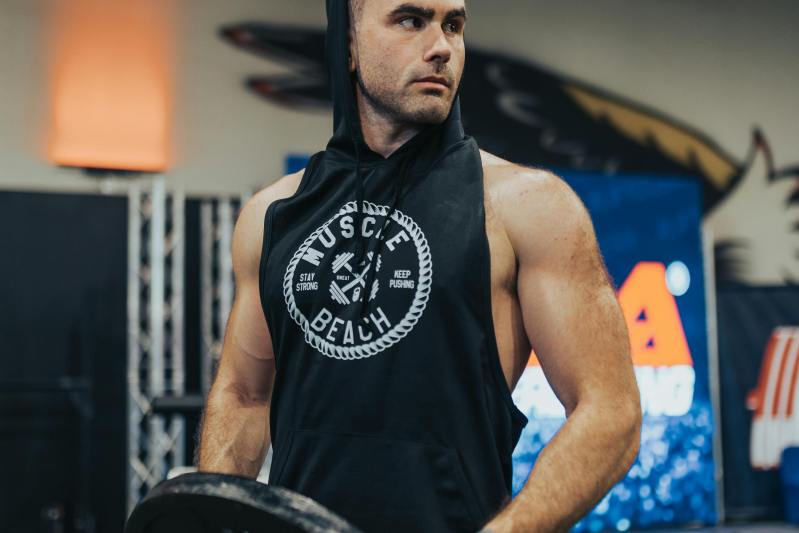 man in gym wearing black sleeveless shirt with hood holding weight