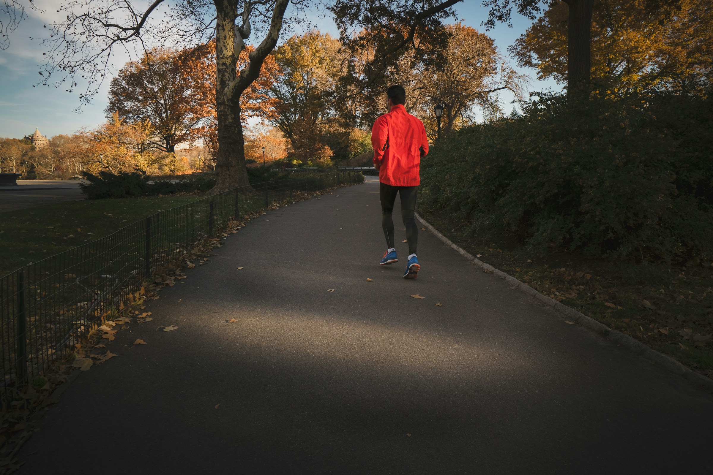 man running through trees on path wearing red jacket